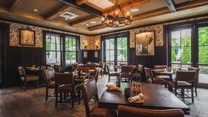 A restaurant with wooden tables and chairs, large windows, and a chandelier. - Kimpton Taconic Hotel by IHG (Manchester)