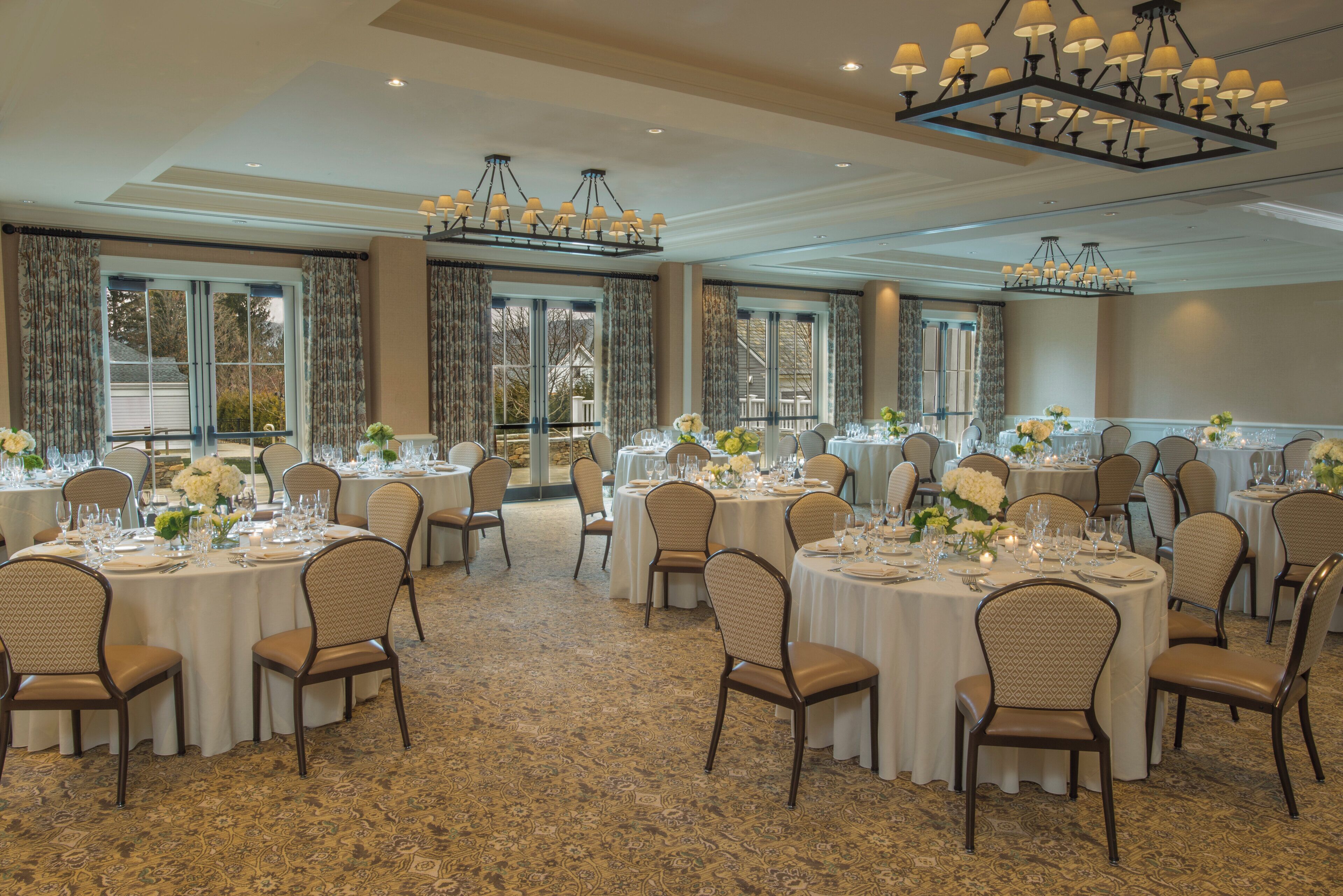 A banquet hall with round tables, chairs, and chandeliers.