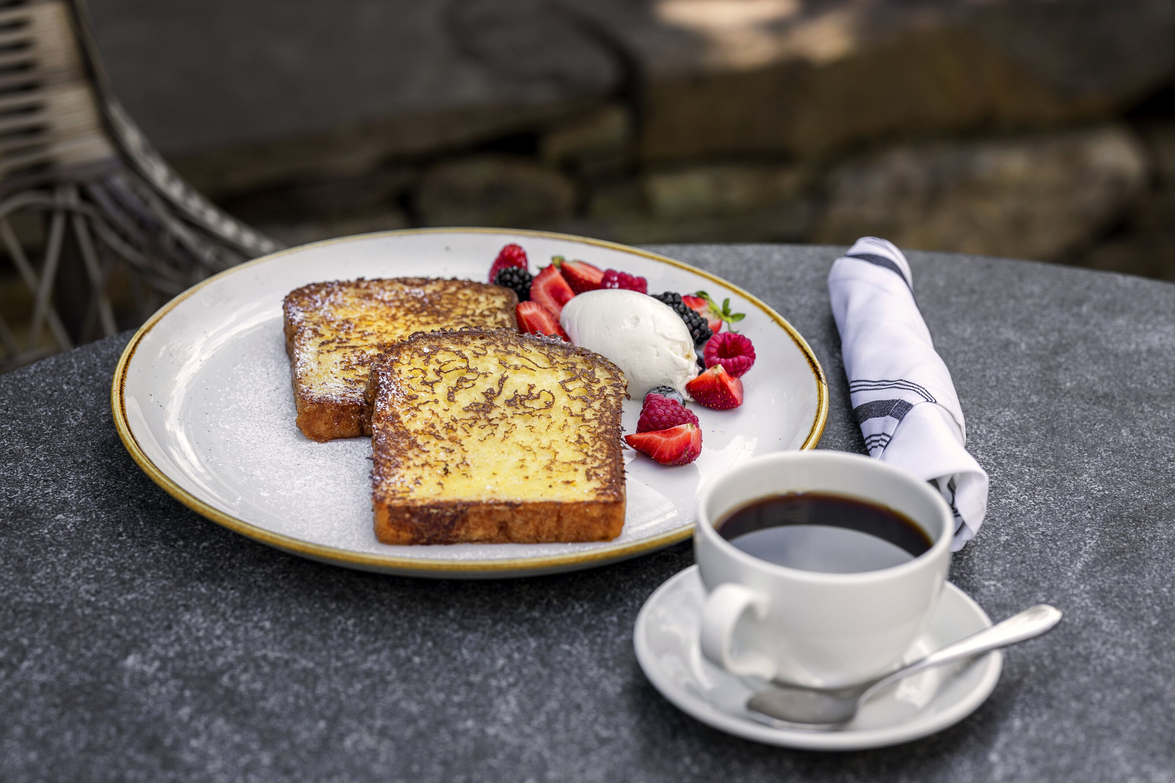 A breakfast setting with French toast, berries, ice cream, and coffee on a table.