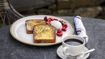 A breakfast setting with French toast, berries, ice cream, and coffee on a table.