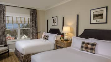 A hotel room with two beds, a nightstand with a lamp, a chair, and a window with curtains.