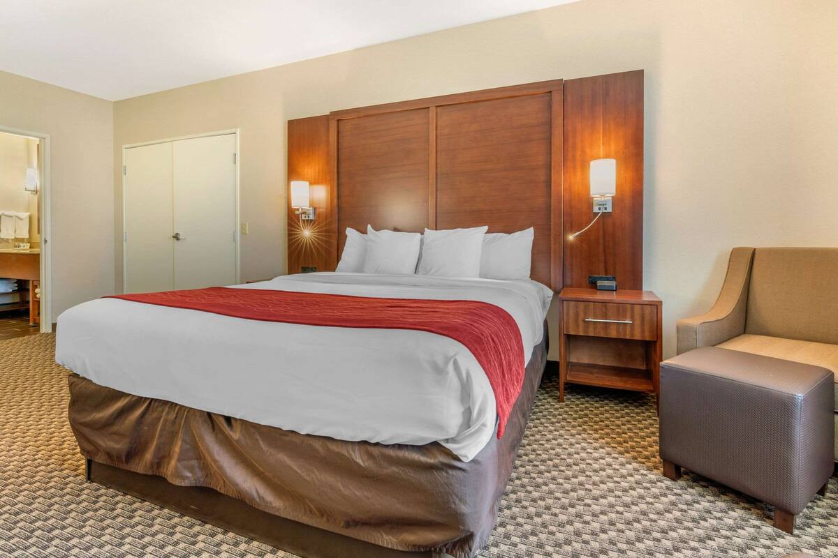 A hotel room with a large bed, a nightstand, a chair, and a wardrobe.