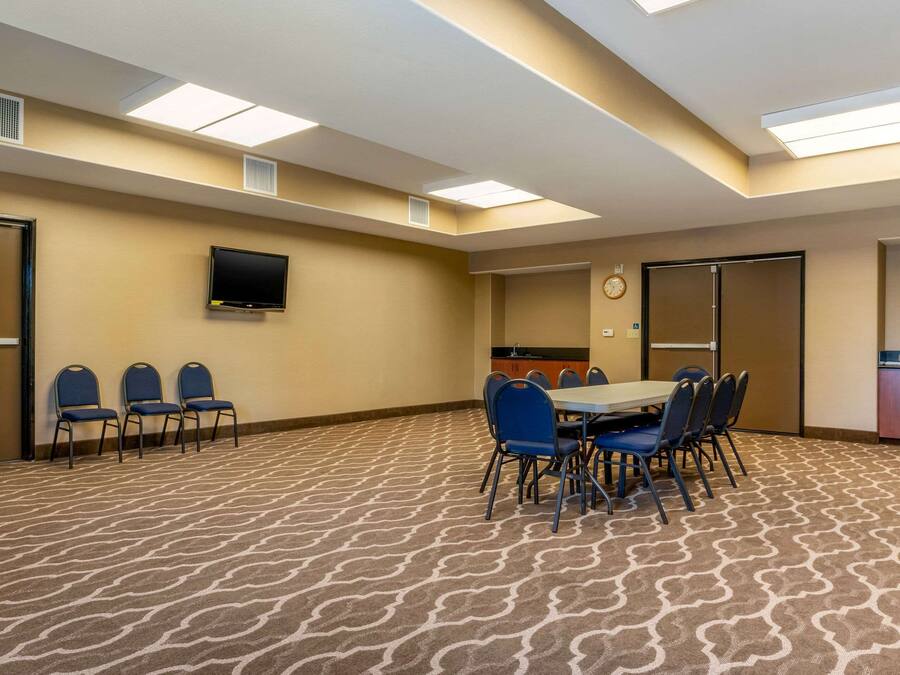 A conference room with a patterned carpet, a flat-screen TV mounted on the wall, a clock, and a kitchenette area.