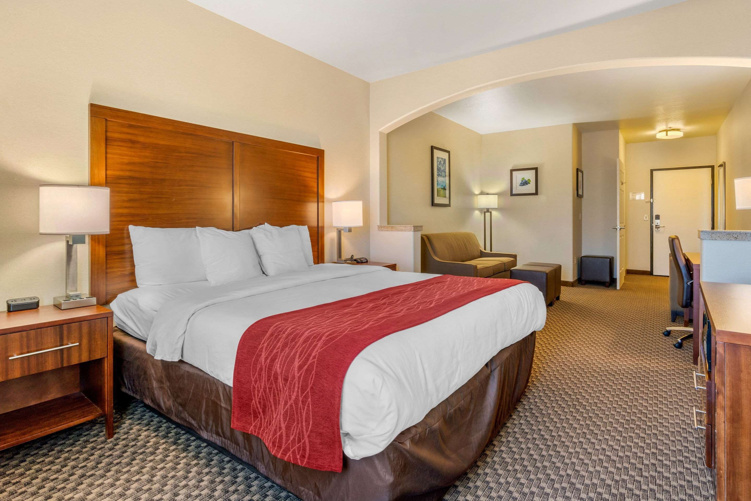 A hotel room with a large bed, a desk, a chair, and a desk lamp.