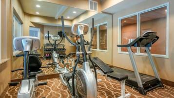 Une salle de sport équipée de machines de cardio, d’un tapis de course et d’un mur avec des miroirs.