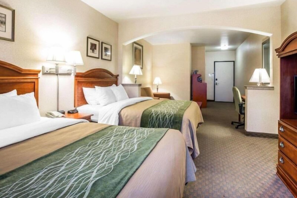 Habitación de hotel con dos camas, un escritorio, una cómoda y un baño visible al fondo.