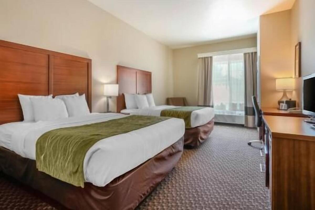 A hotel room with two beds, a desk, a TV, and a window with curtains.