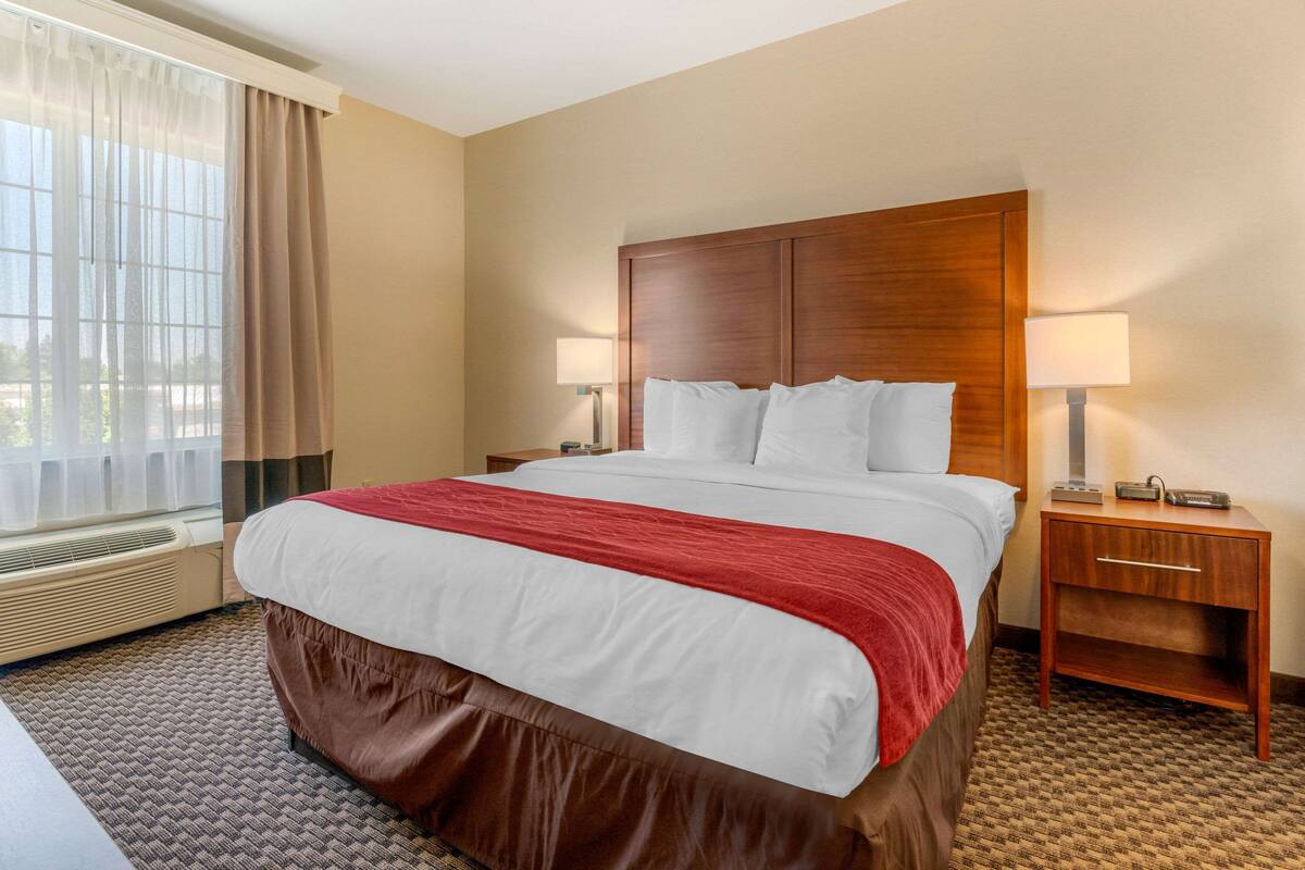 A hotel room with a large bed, two bedside lamps, a wooden nightstand, and a window with curtains.