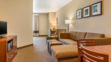 Habitación de hotel con sofá, reposapiés, mesa de madera, televisor y cuadros en la pared.