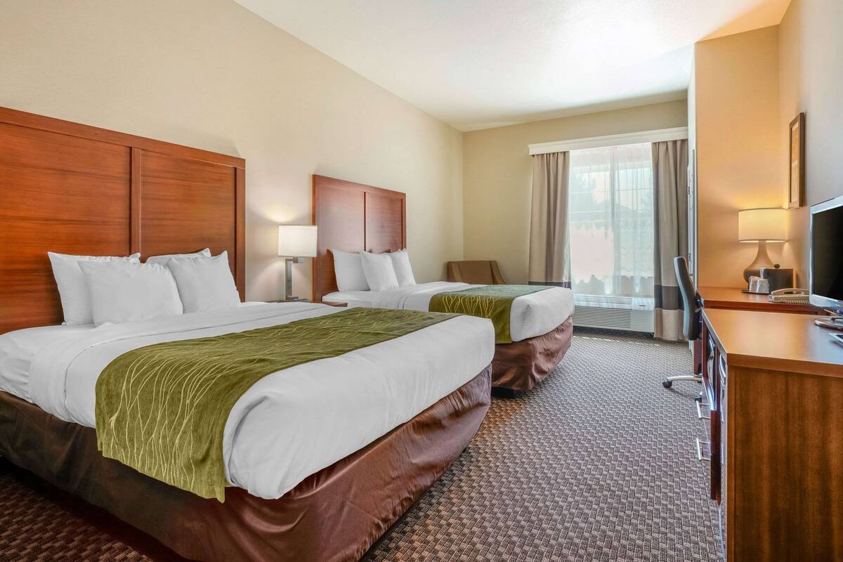 A hotel room with two beds, a desk, a TV, and a window with curtains.