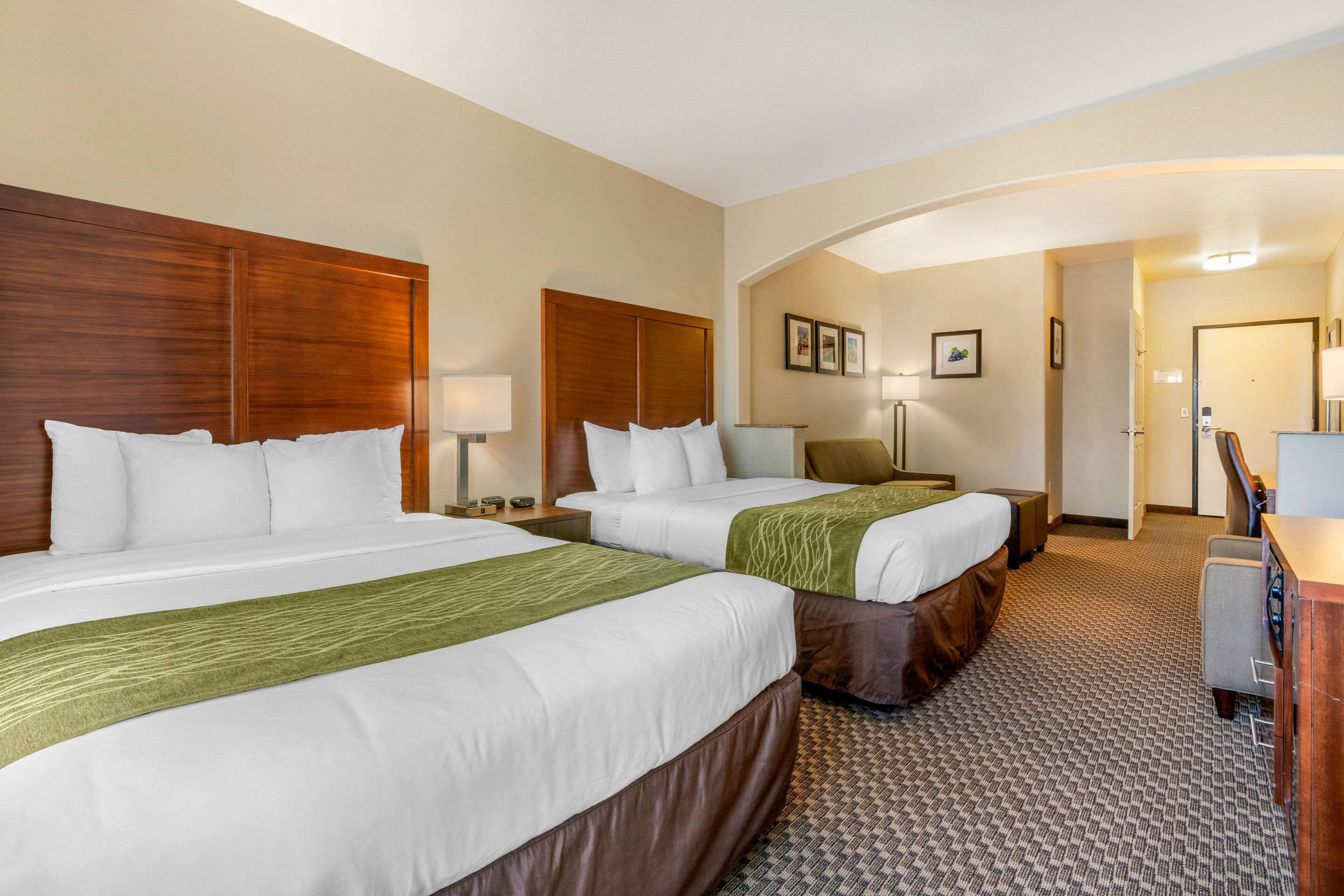 Habitación de hotel con dos camas, un escritorio, una silla y una puerta que da a otra habitación.