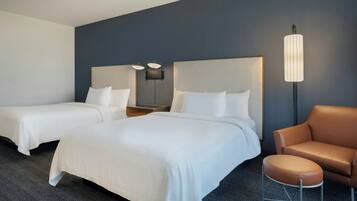 A hotel room with two beds, a brown leather chair, and a modern lamp.