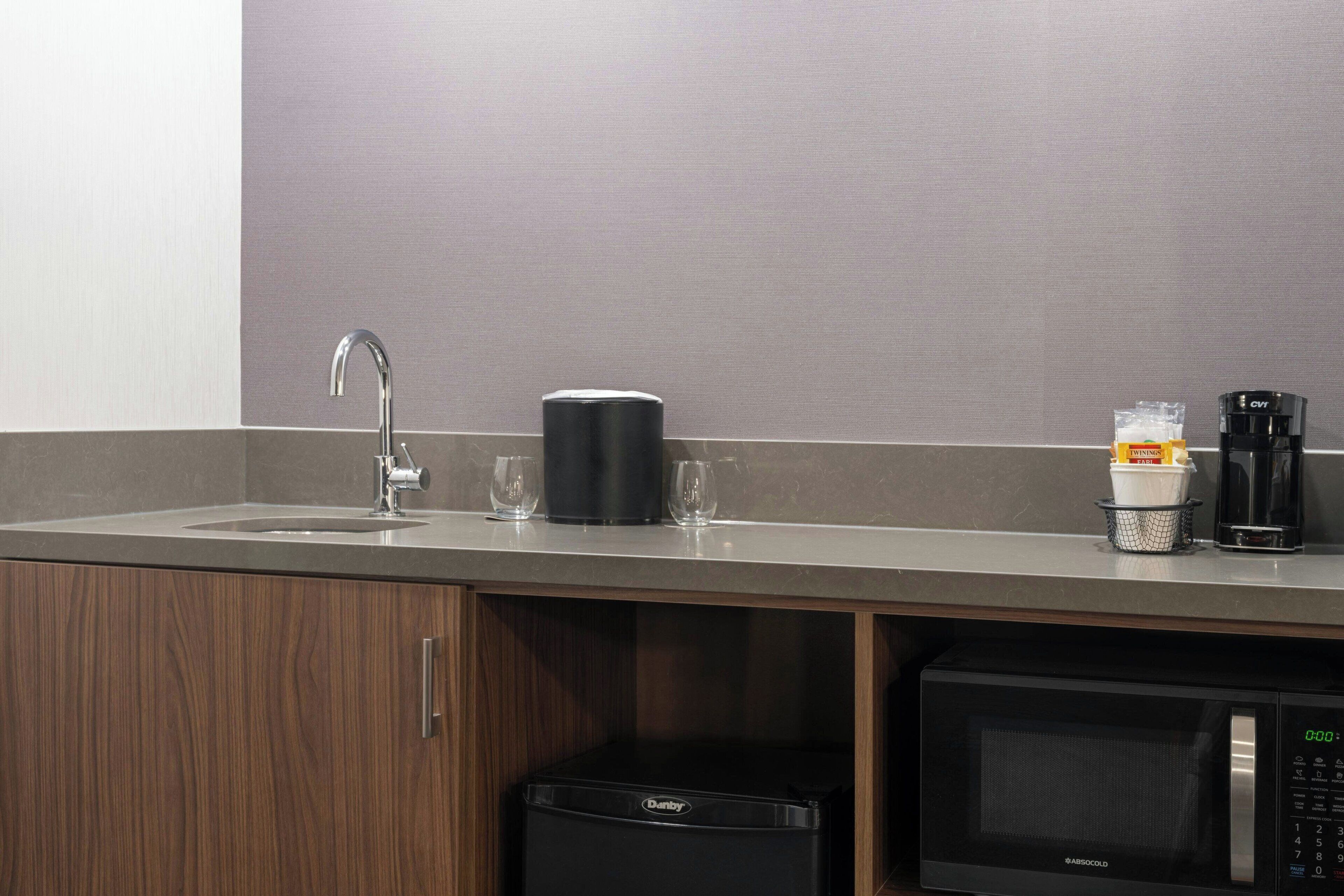 Una kitchenette equipada con microondas, cafetera y una taza de café.
