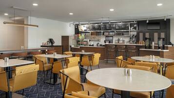 Un restaurante moderno con mesas redondas y sillas amarillas, una barra con menú y una zona de cocina.