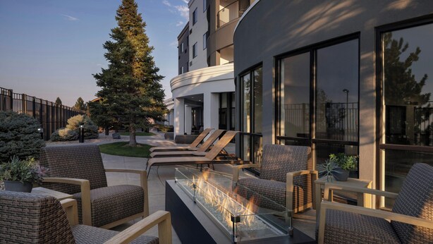 Un espacio exterior moderno con mobiliario de mimbre y una chimenea con superficie de vidrio.