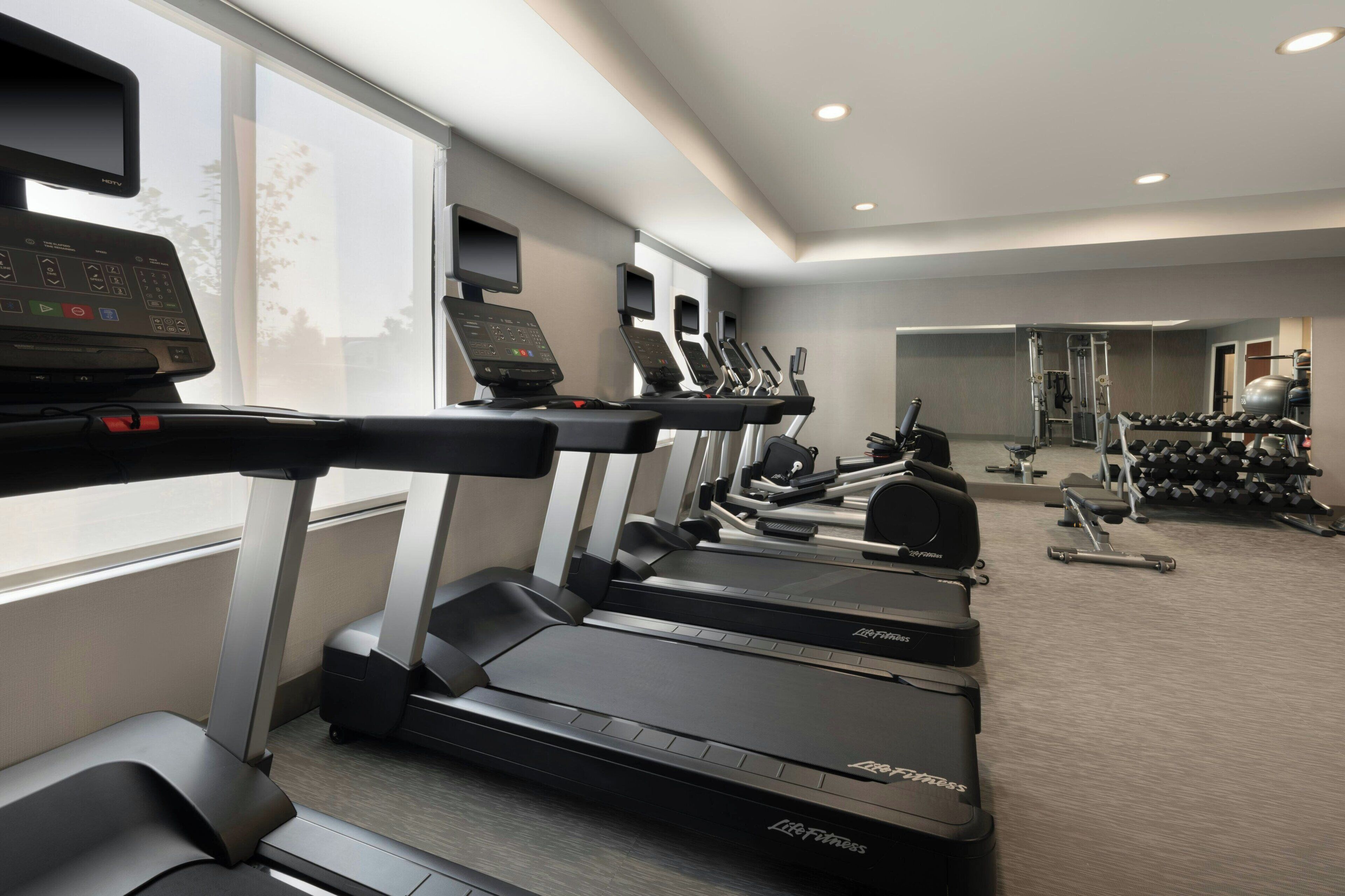 A gym with treadmills, weight machines, and dumbbells.
