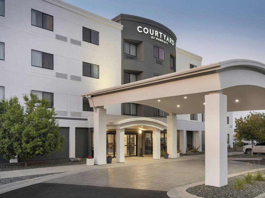 A Courtyard by Marriott hotel entrance with a covered walkway, large windows, and a parking area.