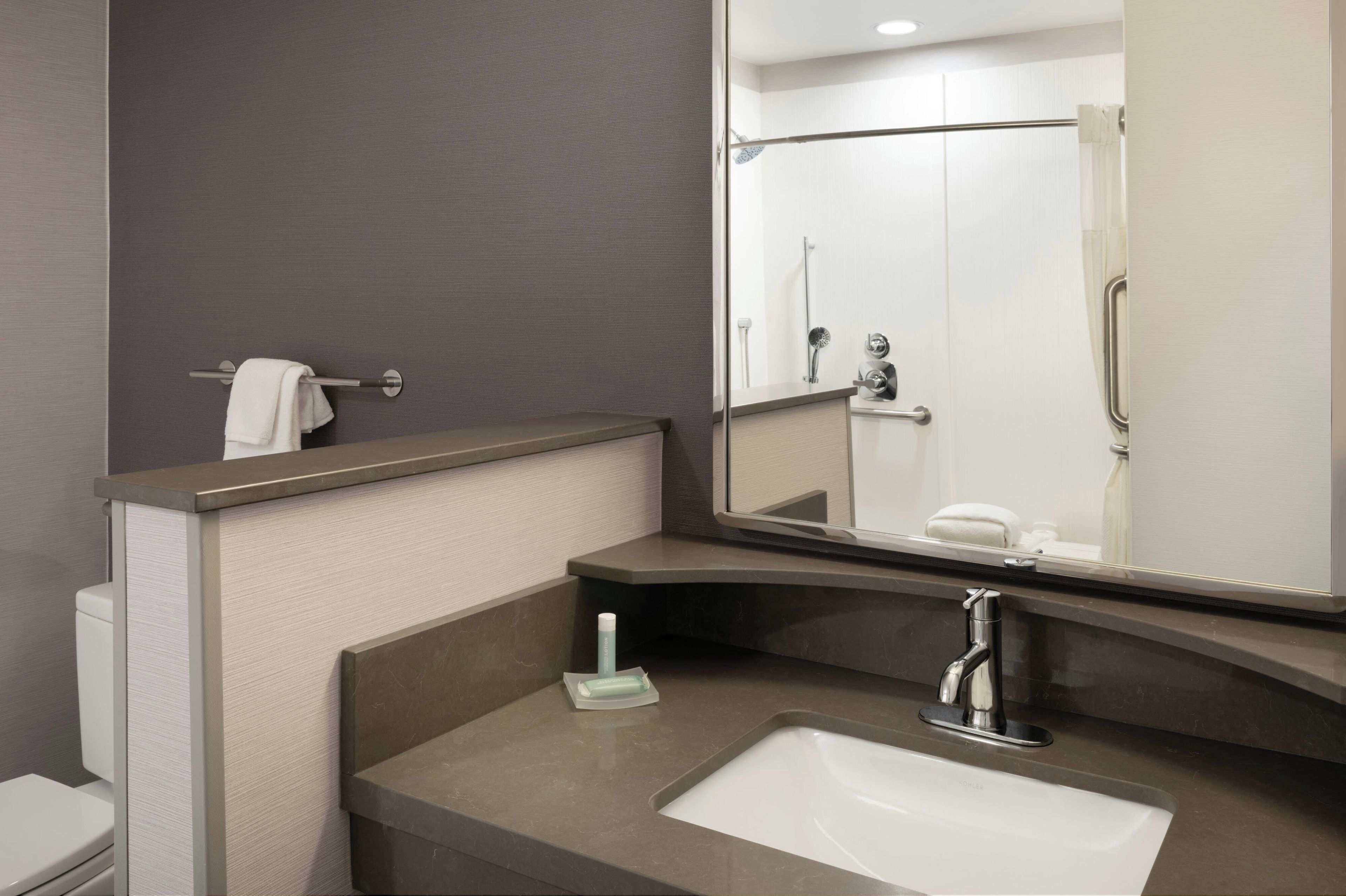 Un baño moderno con un lavamanos blanco, un espejo y una ducha que se ve en el reflejo.