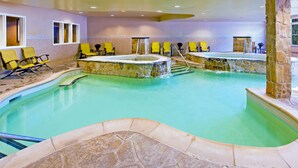 Una piscina amplia en el interior con varias zonas de estar y un jacuzzi.