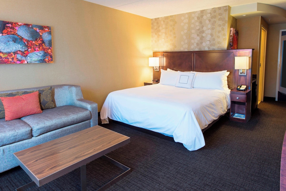 Habitación de hotel con cama, sofá, mesa de centro y un cuadro en la pared.