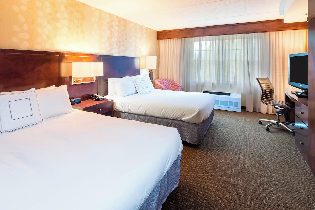Habitación de hotel con dos camas, televisión, escritorio y ventana con cortinas.
