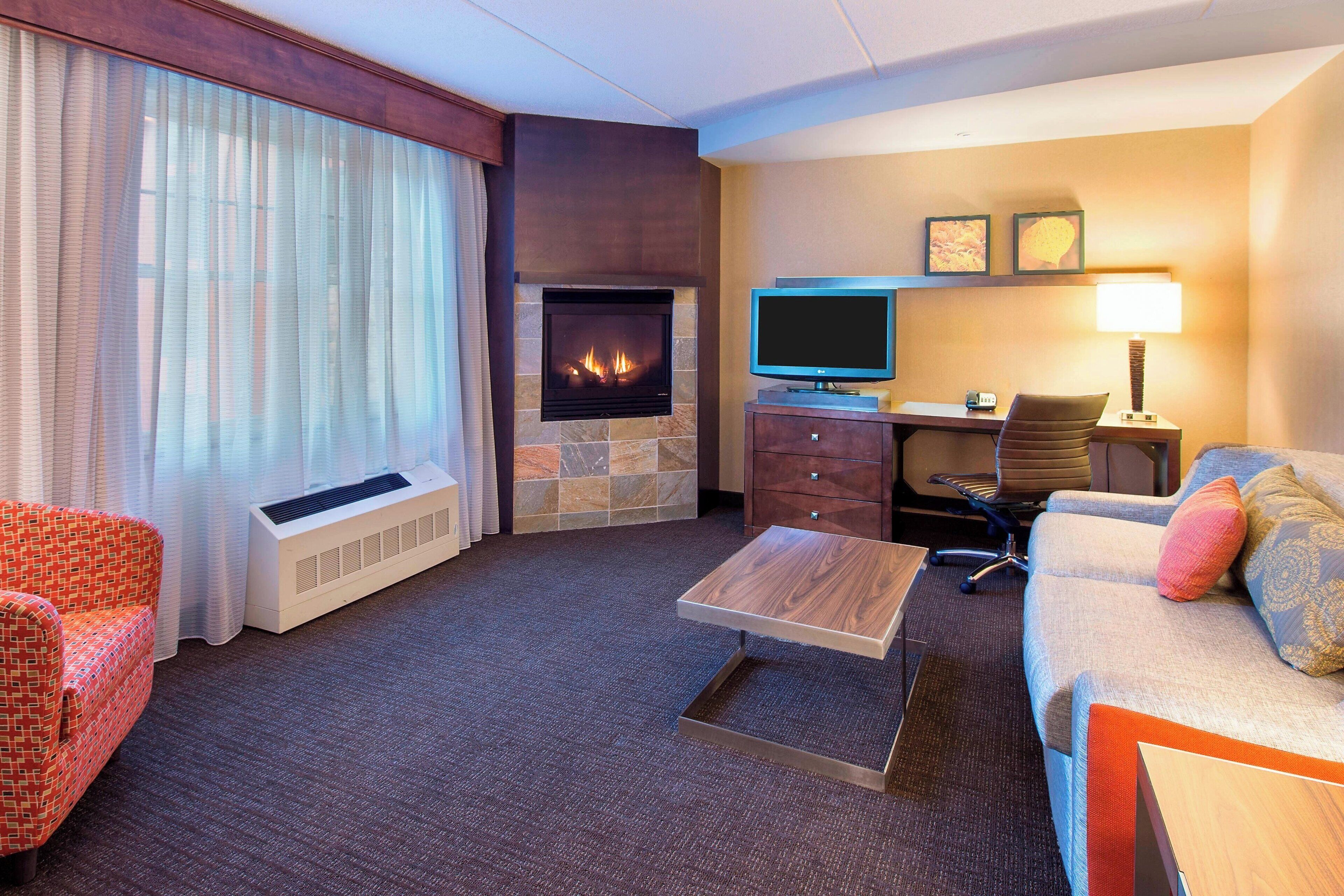 Una habitación de hotel con chimenea, televisor, escritorio, sofá y sillón.