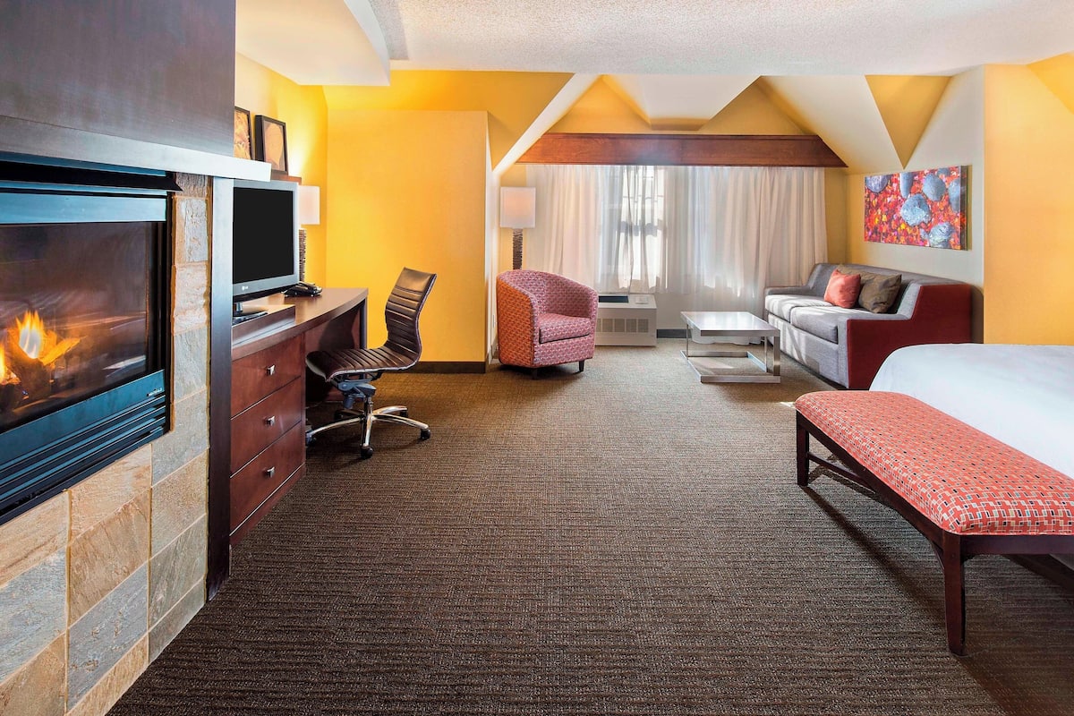 Habitación de hotel con chimenea, sofá, cama, escritorio y una silla.