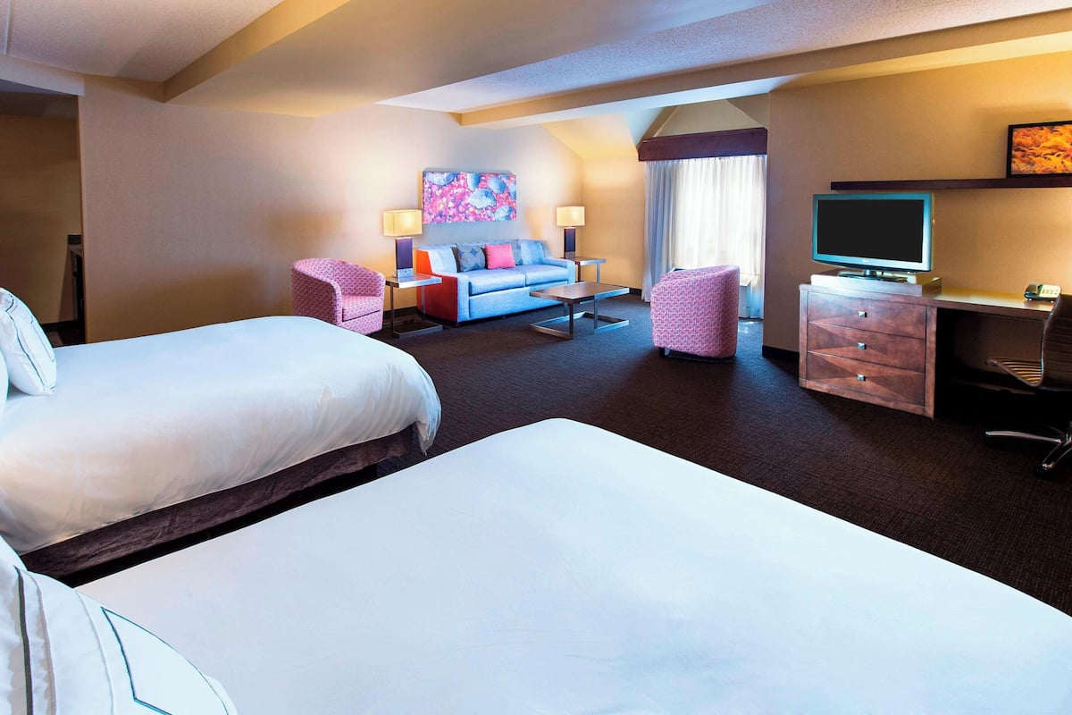Habitación de hotel con dos camas, un sofá, un escritorio, un televisor y un cuadro en la pared.