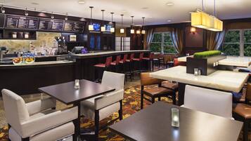 A modern hotel lobby with a bar area, seating arrangements, and a view of the outdoors.