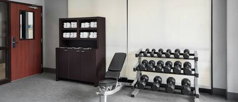 A gym with a bench, dumbbells, and a storage cabinet.
