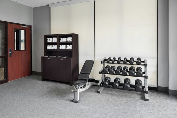 Un gimnasio con una banca, mancuernas y un armario de almacenamiento.