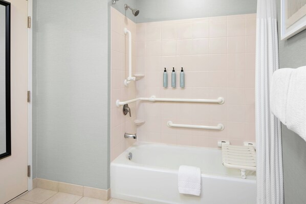 A bathroom with a bathtub, grab bars, and a towel rack.
