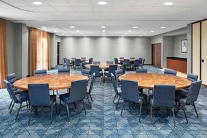 Sala de conferência com mesas e cadeiras redondas, piso coberto por carpete e iluminação embutida.