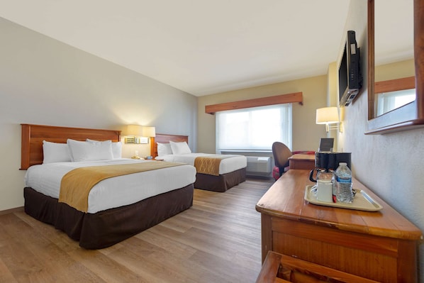 Une chambre d’hôtel avec deux lits, un bureau avec un plateau d’eau et une machine à café, et un téléviseur fixé au mur.