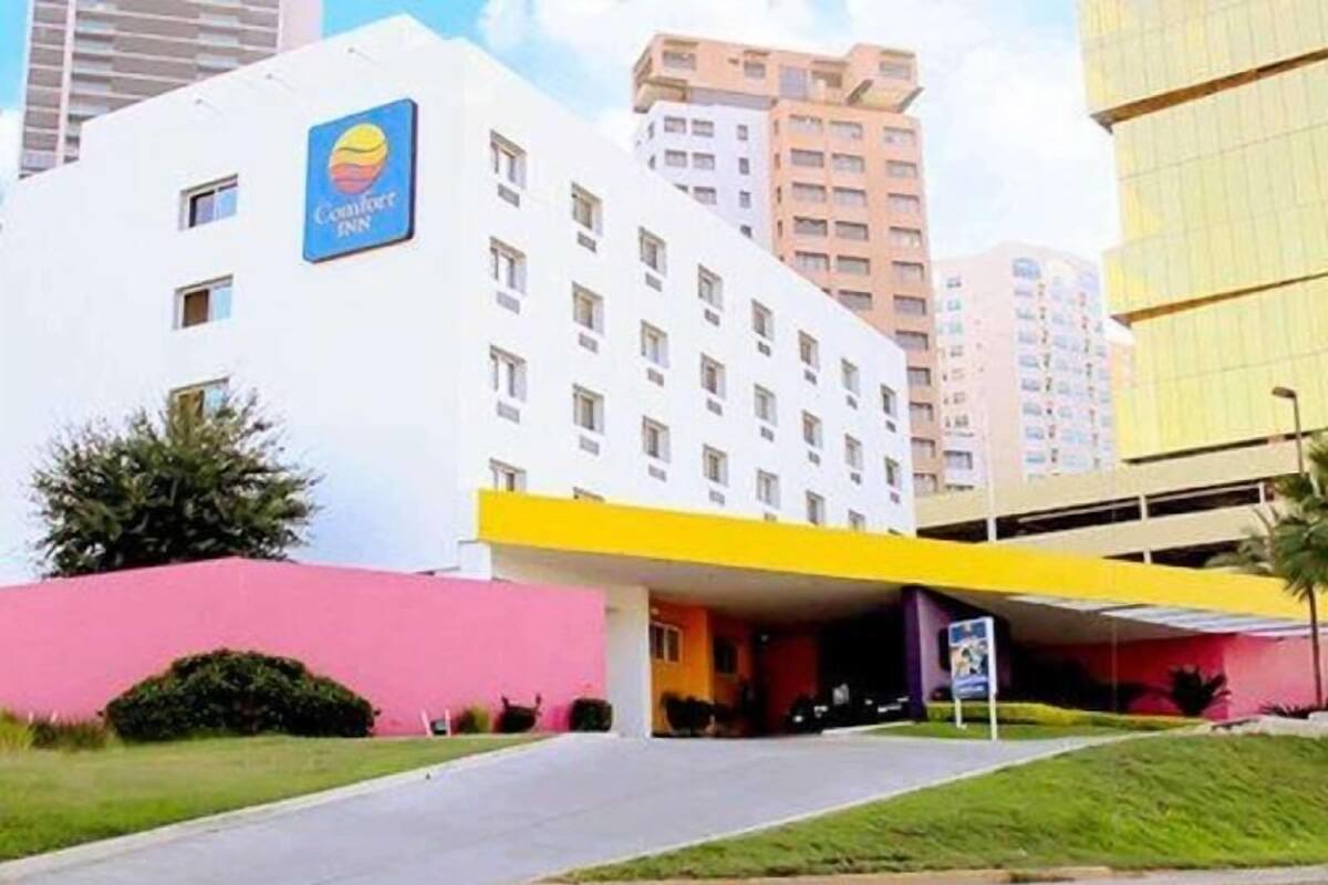 Un hotel con un letrero llamativo, un acceso cubierto y una construcción para estacionamiento.