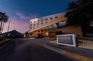 Un hotel de diseño moderno, con un letrero que indica la dirección '1009 Lázaro Cárdenas' y una montaña al fondo.