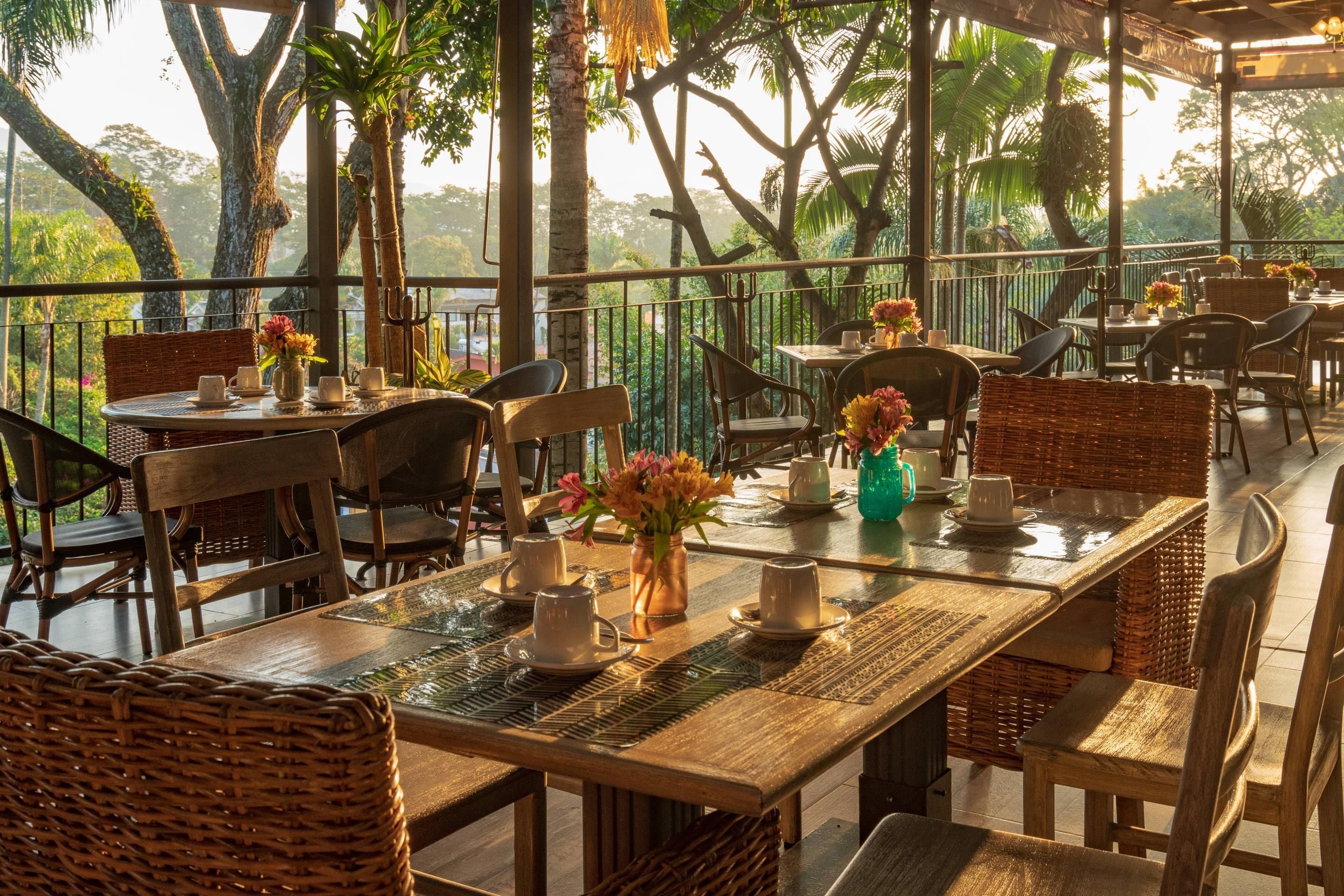 Un área de comedor al aire libre con mesas y sillas, rodeada de árboles y una barandilla.