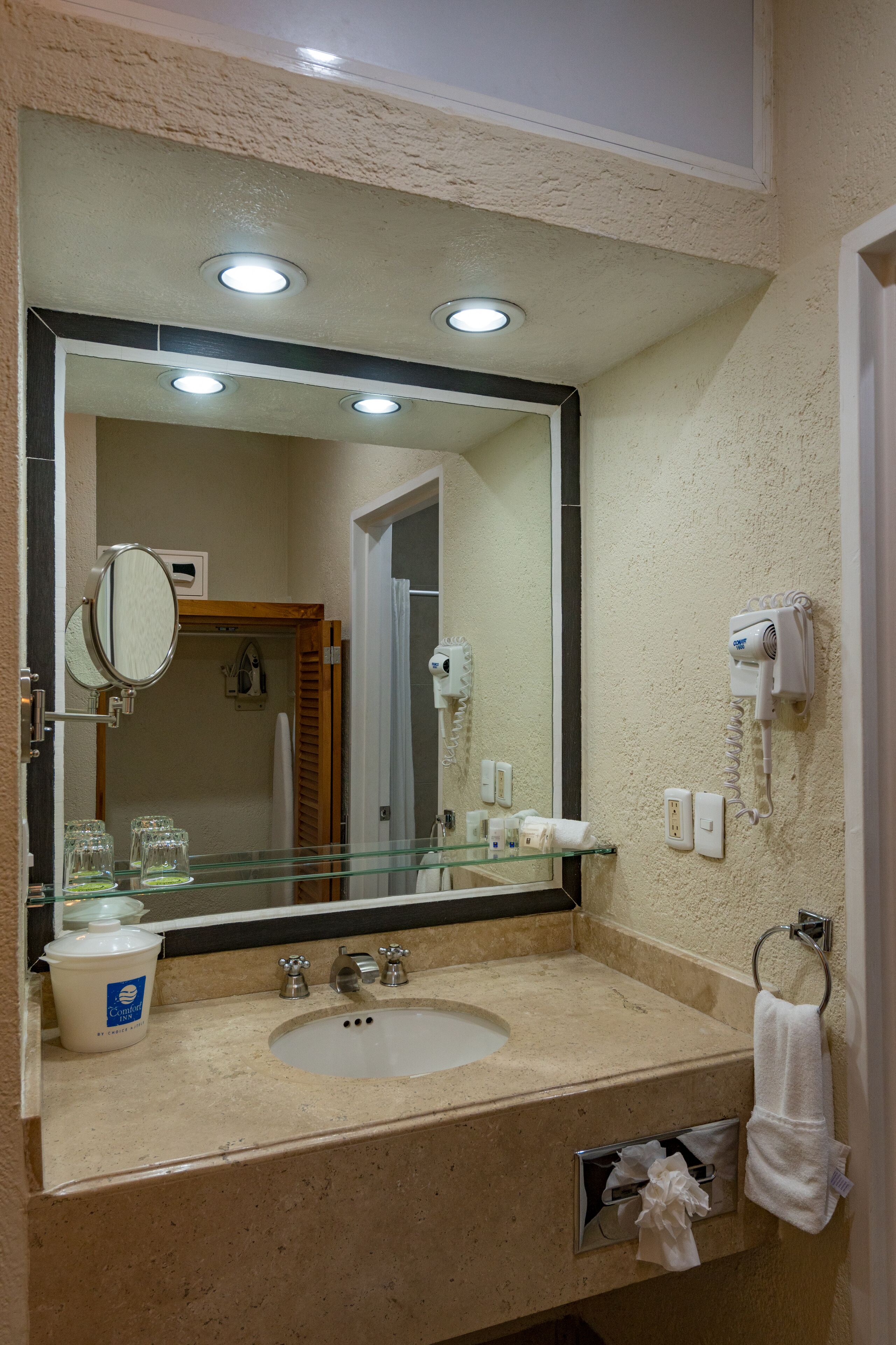 A bathroom with a large mirror, a sink, a glass shelf, a hairdryer, and a towel rack.