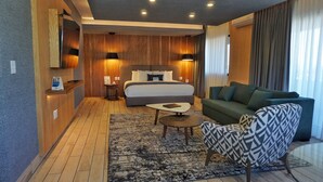 A modern hotel room with a large bed, a green sofa, a patterned armchair, a small coffee table, and a wooden accent wall. - Comfort Inn Cordoba (Córdoba)