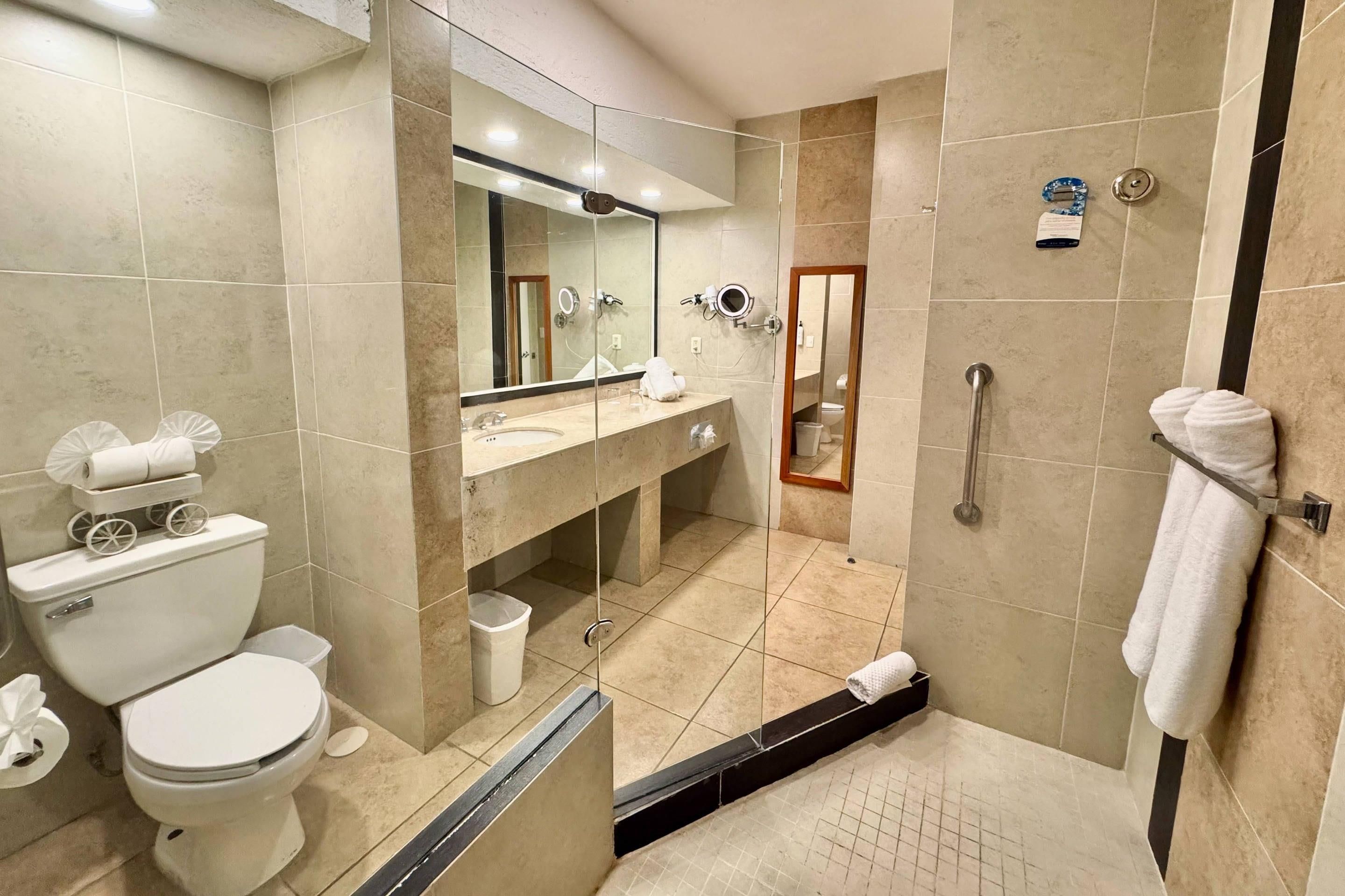Un baño de hotel con inodoro, lavamanos, espejo y zona de ducha.