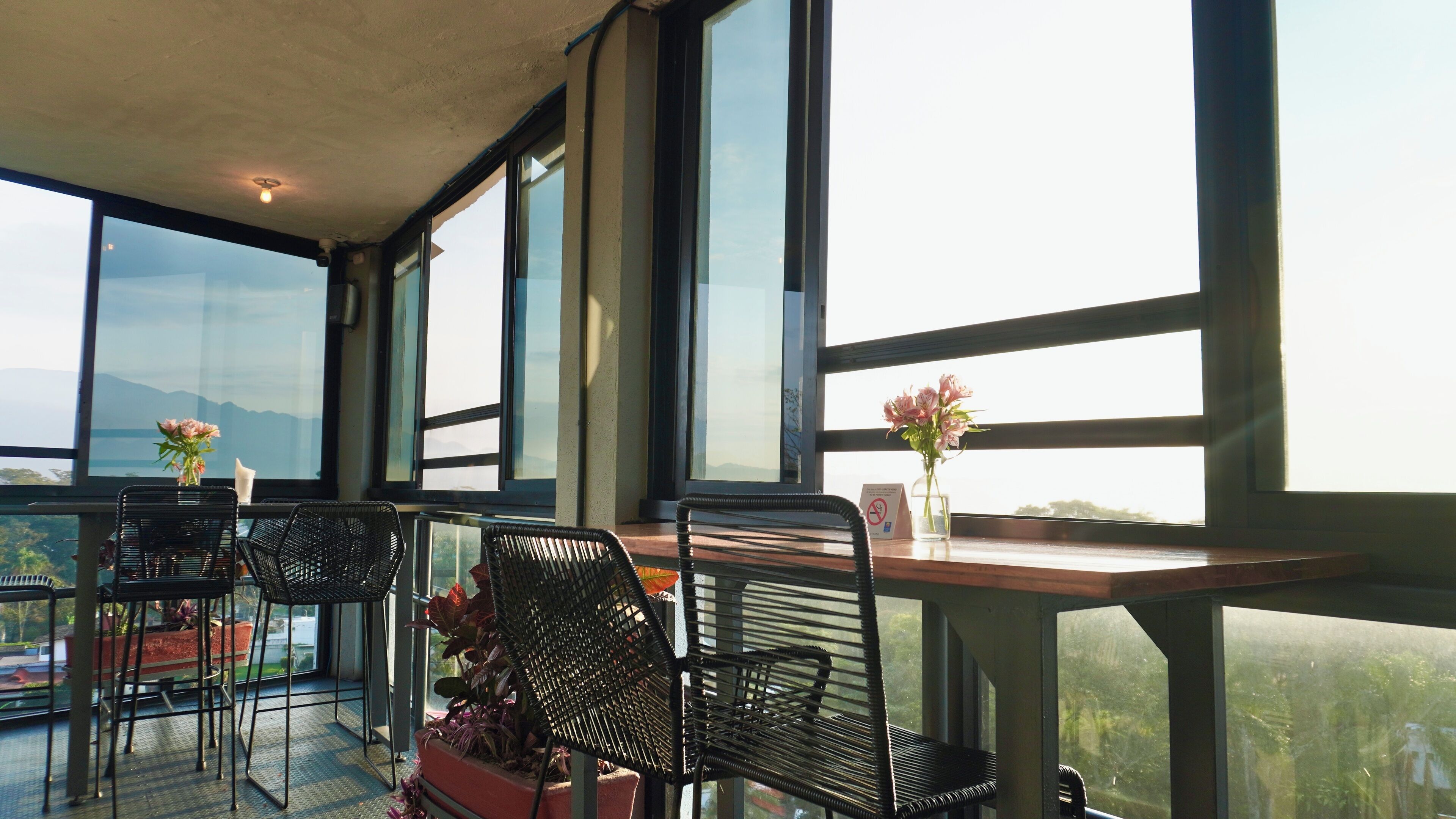 A high-rise room with large windows, two chairs, a table, and a vase with flowers.