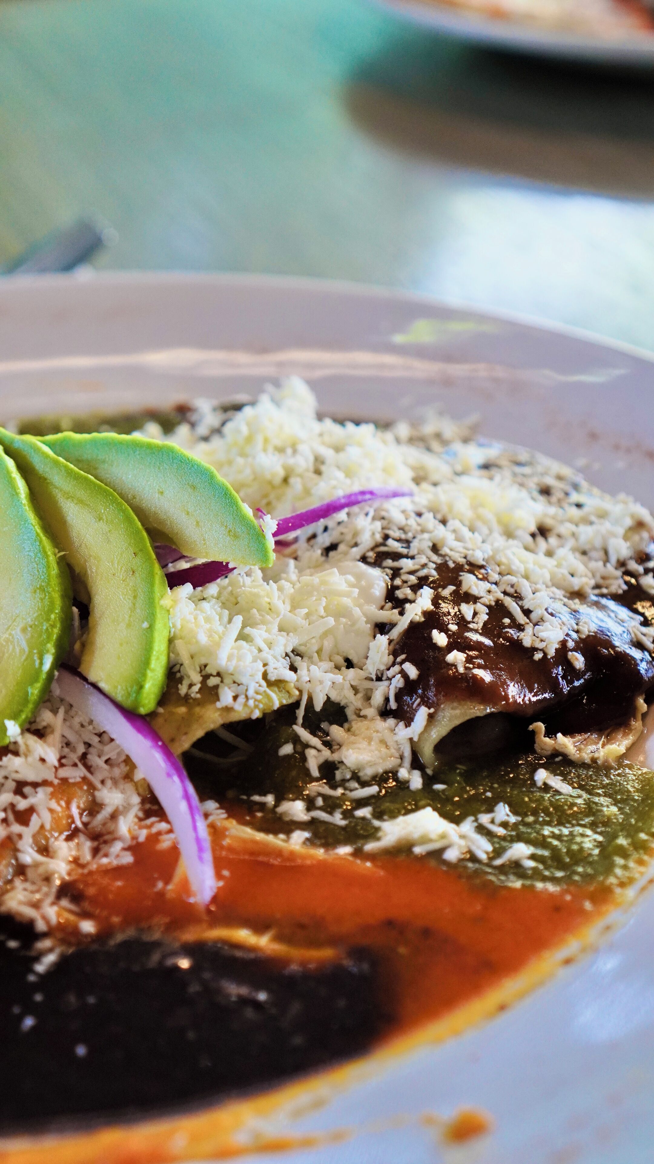 A plate of food with a green sauce, rice, avocado slices, and a red onion.