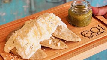 Una tabla de madera con un plato de nachos cubiertos de queso y un frasco pequeño de salsa verde.