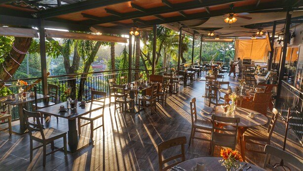 An outdoor restaurant with wooden tables and chairs, surrounded by lush greenery. - Comfort Inn Cordoba (Córdoba)