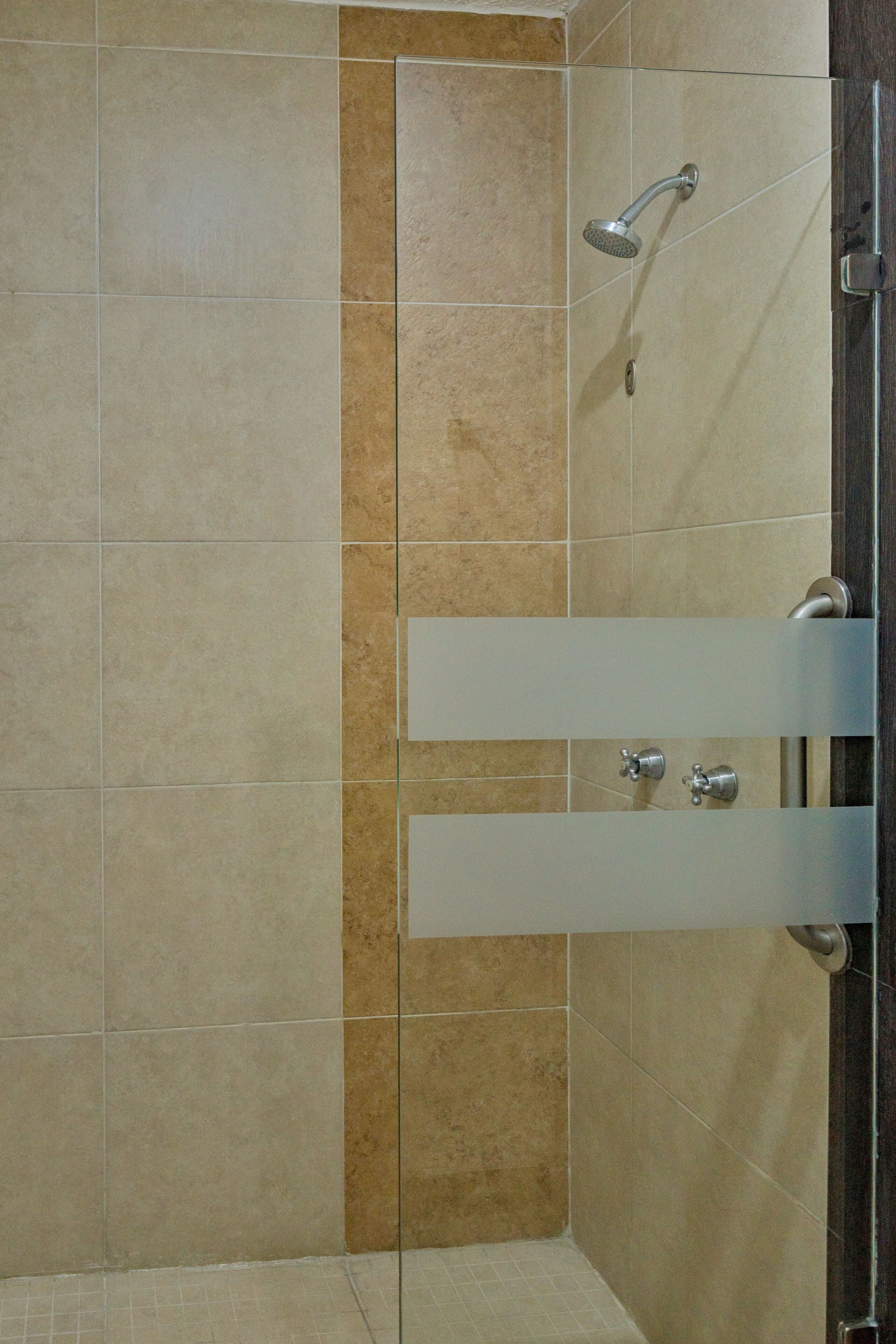A shower area with beige tiles and a glass door.