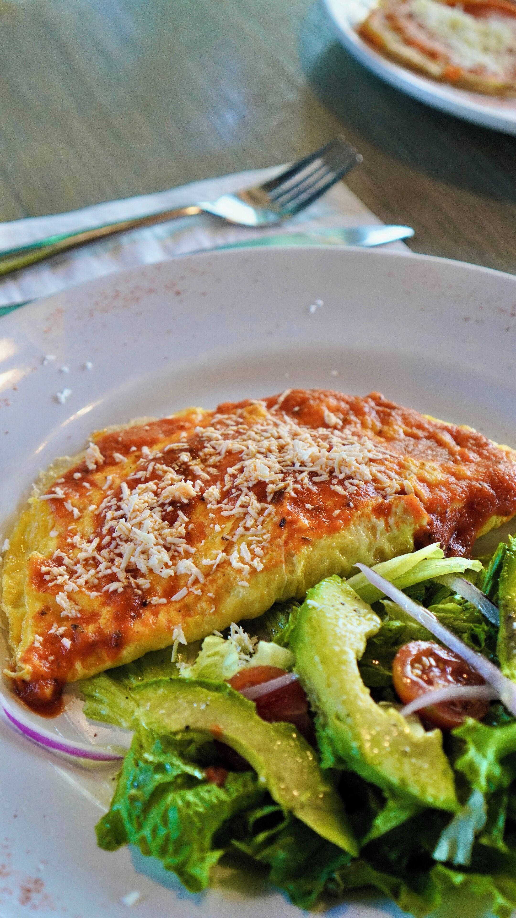 Un plato con una porción de pizza cubierta de queso y una ensalada al lado.