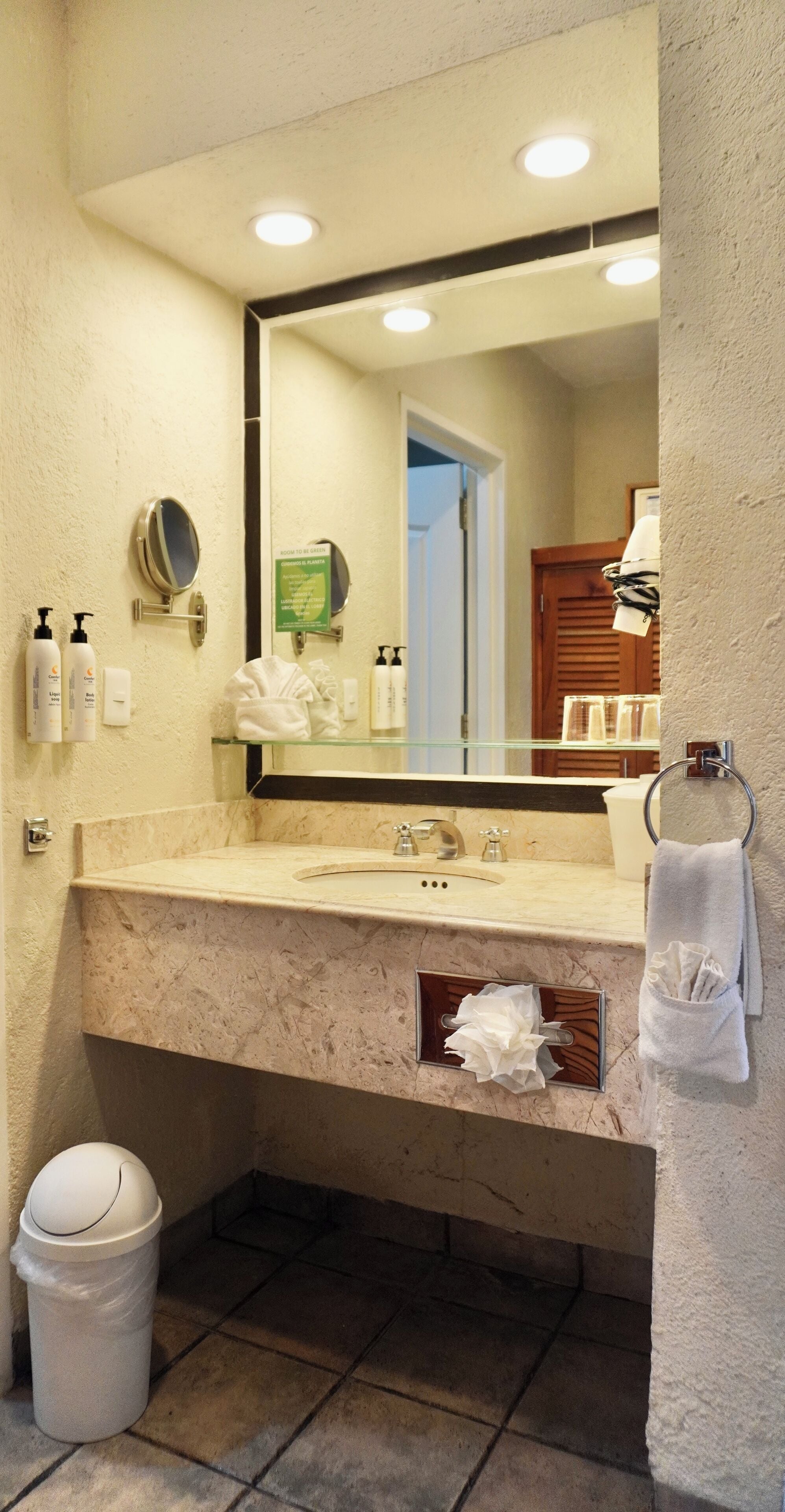 A bathroom with a marble sink, a mirror, a towel rack, and a trash bin.