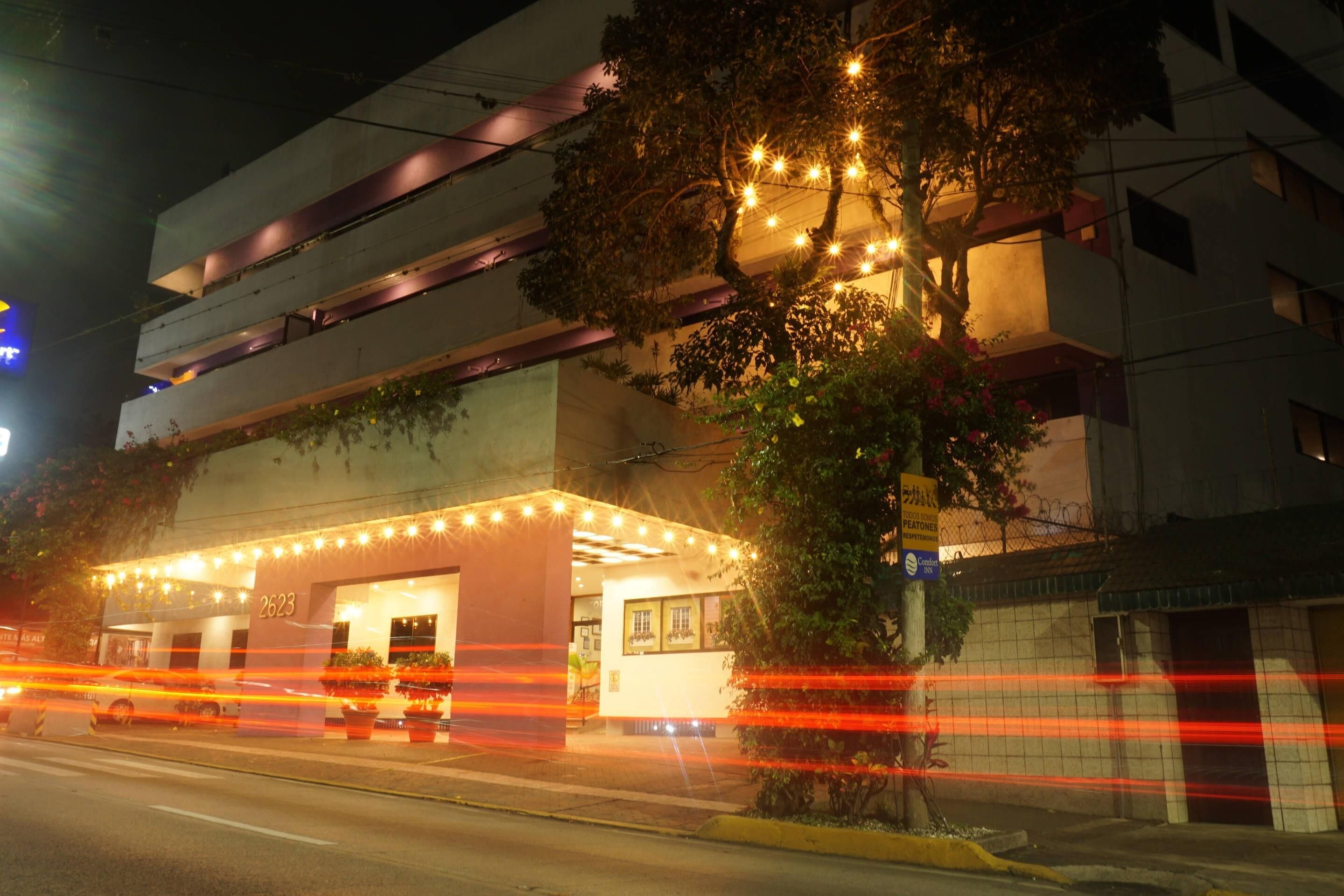 Un edificio con un cartel que indica el número 2623, una zona de acceso cubierta con luces y un árbol en frente.