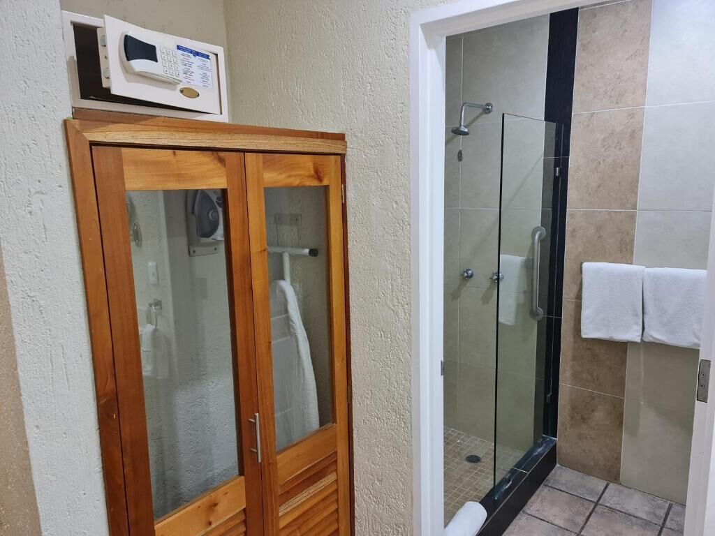 A bathroom with a wooden cabinet, a glass shower enclosure, and a white towel hanging on the wall.