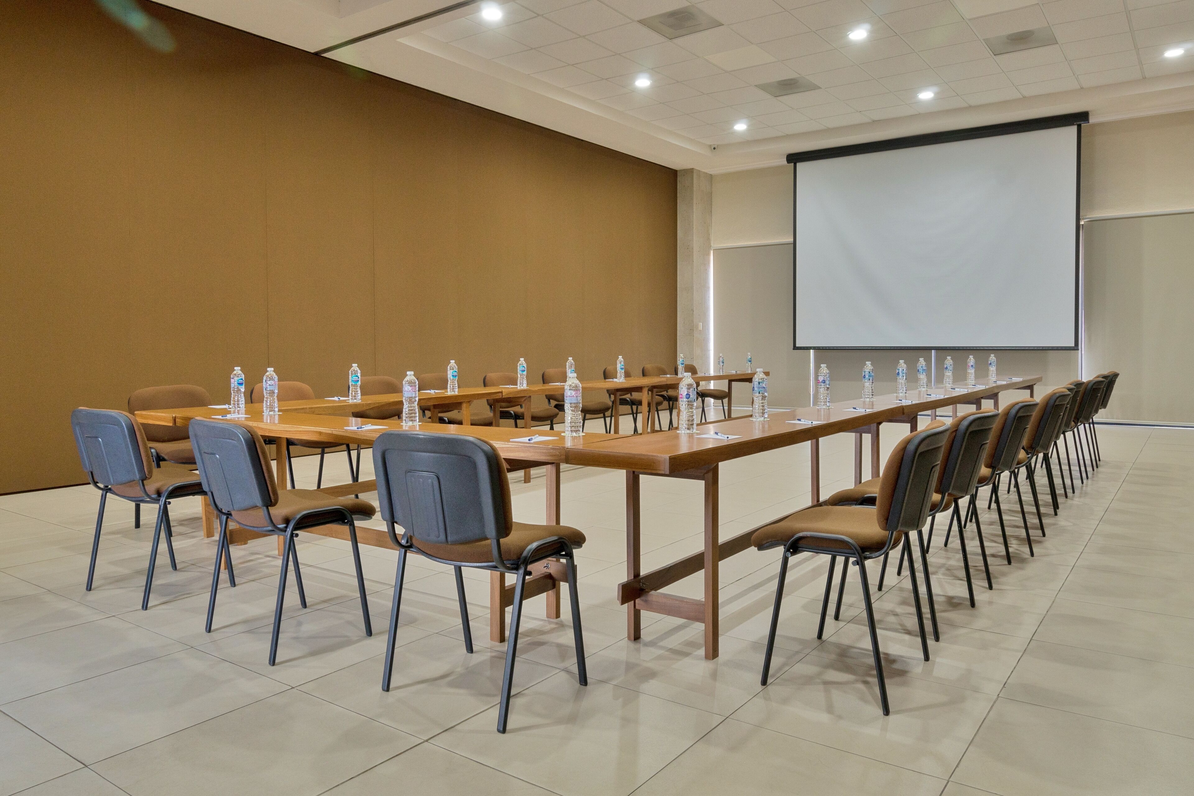 A conference room with long tables, chairs, water bottles, and a projector screen.